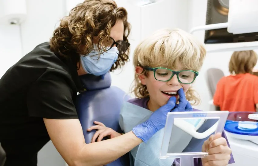 niño mirándose al espejo los dientes con una dentista